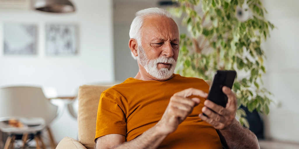 An man uses a smartphone in his modern living room, depicting how AngelSense Assistive Technology helps seniors manage their daily lives independently.