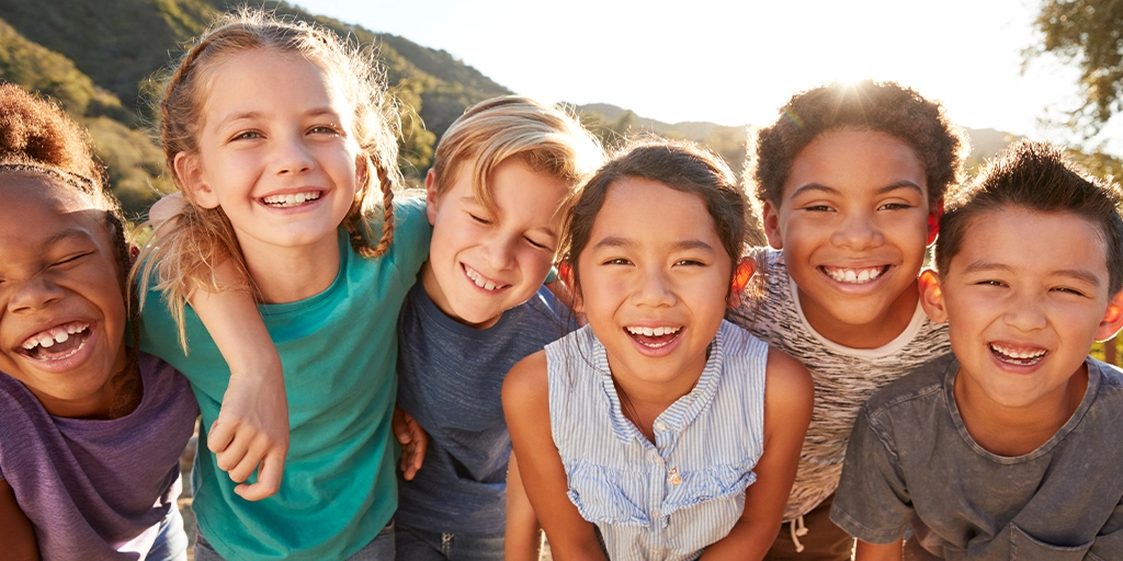 A group of six diverse children, including some with autism, standing close together outdoors, smiling and laughing.