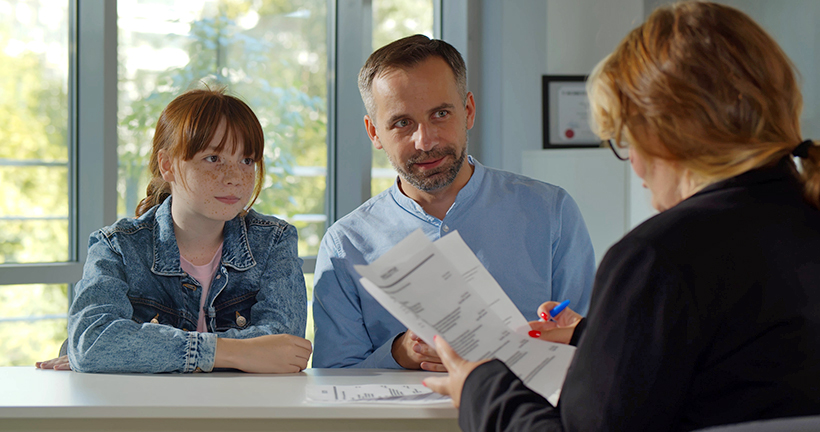 Father and daughter discussing autism support needs with a teacher.